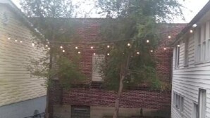 A courtyard with a brick wall, a tree, and string lights. - The House on Wine Alley (Hermann)