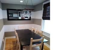 A dining area with a black table and wooden chairs, a hanging light fixture, and a window with blinds. - The House on Wine Alley (Hermann)