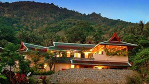 A traditional building with a stone wall and a red roof, surrounded by lush greenery and a hillside.