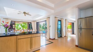 A modern kitchen with a central island, a large refrigerator, and sliding glass doors leading to a balcony with a view of greenery.