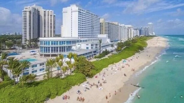 Ein Strandhotel mit mehreren Hochhäusern, einem Poolbereich und einem Sandstrand.