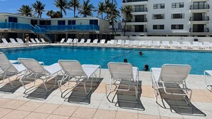 Ein Swimmingpool mit Liegestühlen und Palmen, umgeben von einem mehrstöckigen Gebäude mit Balkonen.