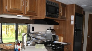 A compact kitchen with wooden cabinets, a microwave, a stove, and a refrigerator.