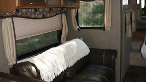 A cozy RV interior with a leather couch, a patterned headboard, and a window with curtains.