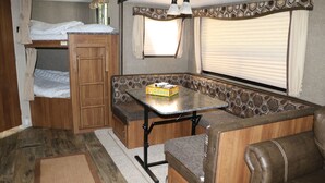 A compact RV interior with a bunk bed, a kitchenette, a dining area, and a seating area.