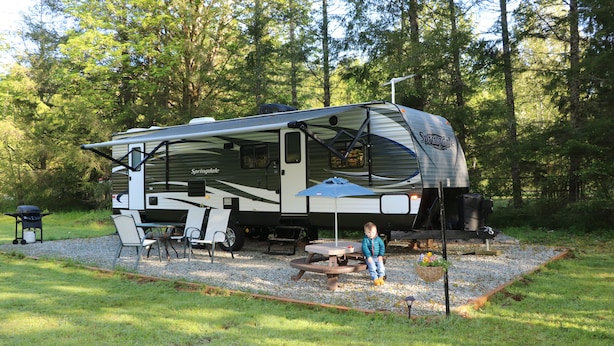 A recreational vehicle (RV) with a covered living area, a picnic table, and a grill.