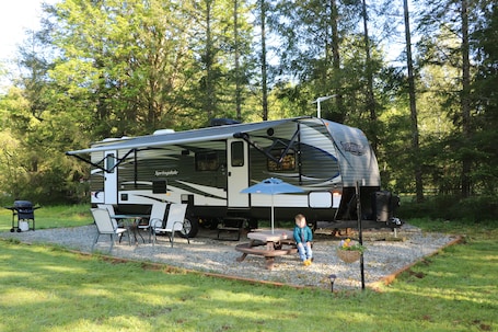A recreational vehicle (RV) with a covered living area, a picnic table, and a grill.