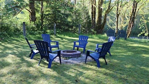 A circular seating arrangement with four chairs around a central fire pit in a grassy outdoor area.