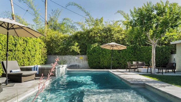 A rectangular swimming pool with a hot tub, surrounded by a patio area with outdoor furniture and umbrellas. - Movie Colony Home with Private Casita, Pool & Spa! (Palm Springs)