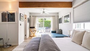 A modern hotel room with a large bed, a seating area with a blue sofa, and a balcony with outdoor furniture. - Movie Colony Home with Private Casita, Pool & Spa! (Palm Springs)