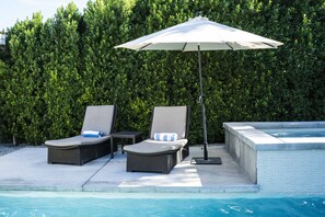 Un área junto a la piscina con dos sillones, una mesa y una sombrilla.
