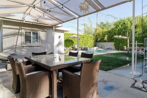 Un patio cubierto con una mesa de vidrio y sillas de mimbre, un jacuzzi y una piscina al fondo.