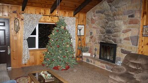 Un salon chaleureux avec une cheminée en pierre, un sapin de Noël et un canapé confortable.