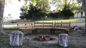 Un banc en bois avec un foyer au centre, entouré d’arbres et d’une clôture.