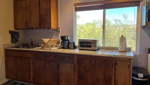 Cucina con mobili in legno, macchina per il caffè, tostapane e una finestra vista alberi.
