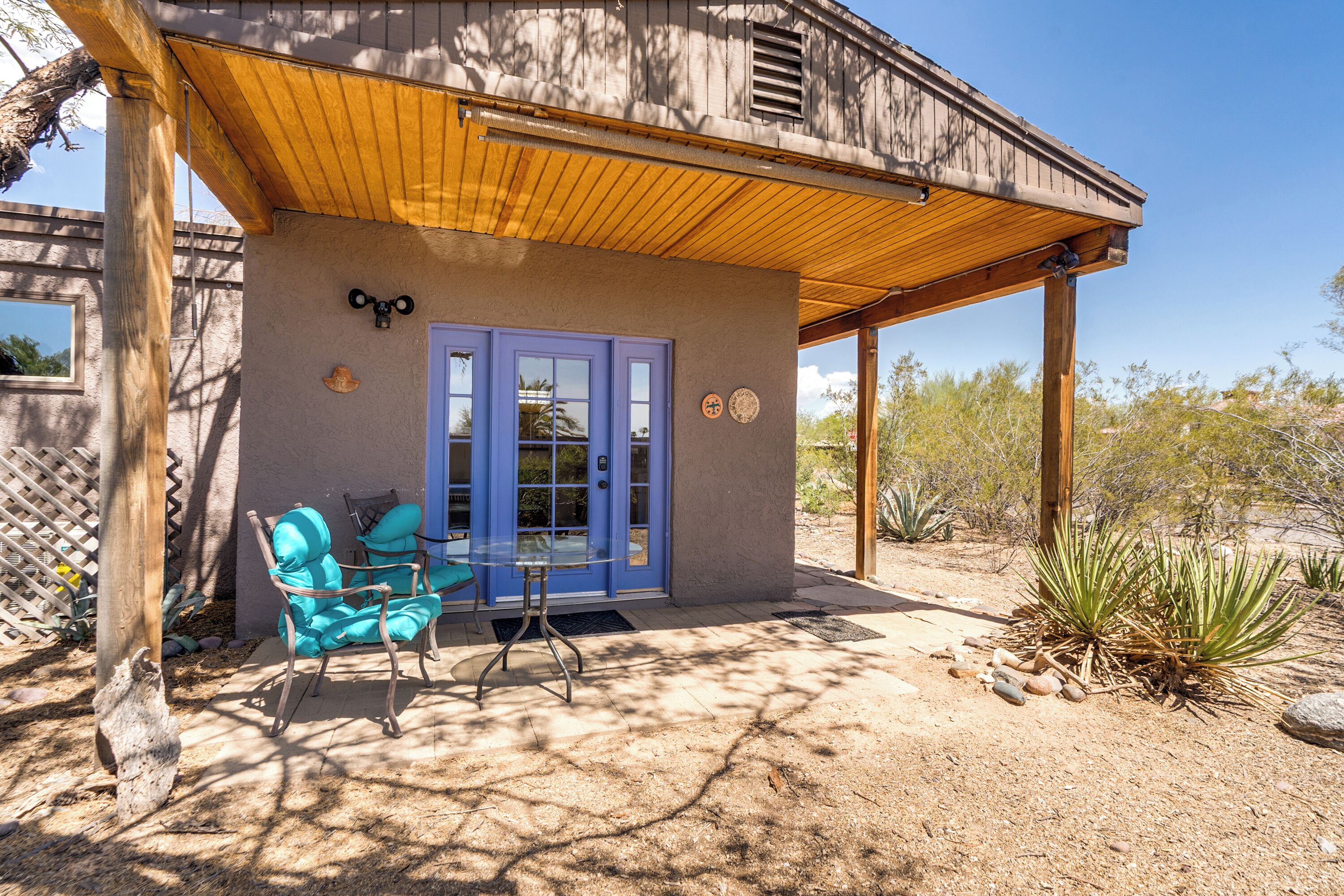 A wooden building with a blue door and a covered patio area with a chair and table.