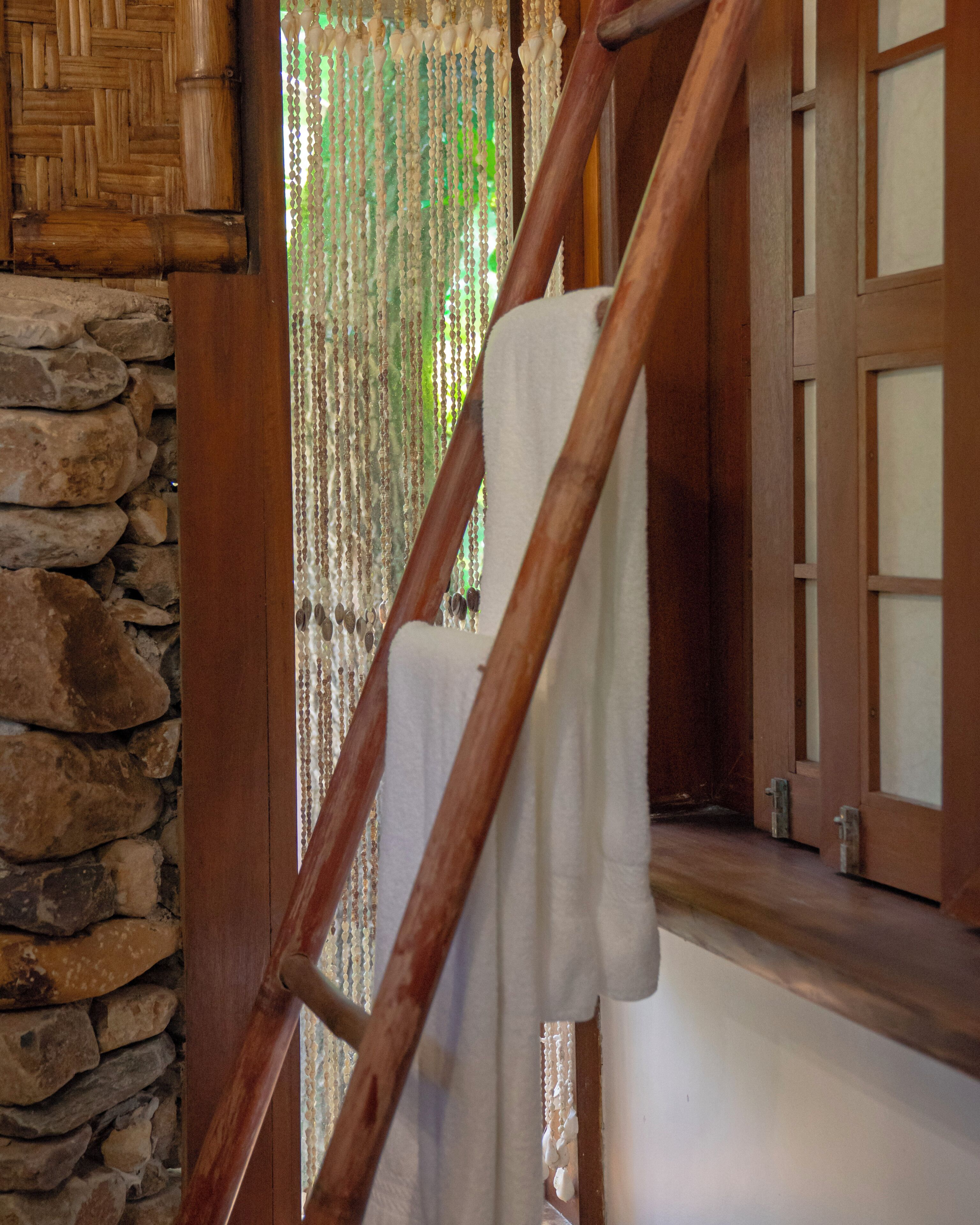 A wooden staircase with a white towel hanging on the railing, a stone wall, and a wooden door with glass panels.