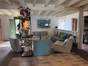 Ein Wohnzimmer mit einer Couch, Sesseln, einem Couchtisch und einem Wandregal mit verschiedenen Gegenständen.