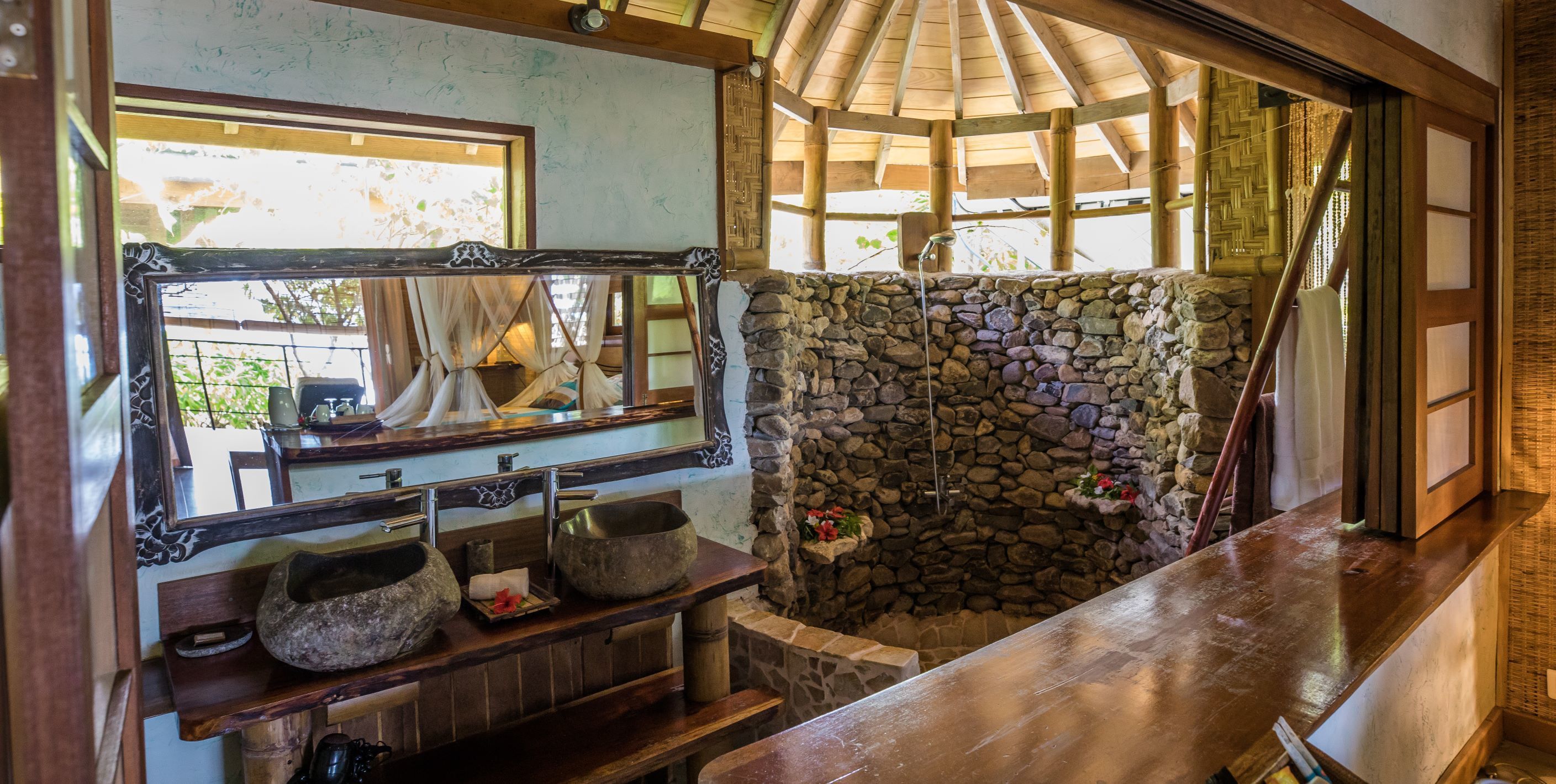 Un baño rústico con pared de piedra, repisas de madera y un espejo grande.