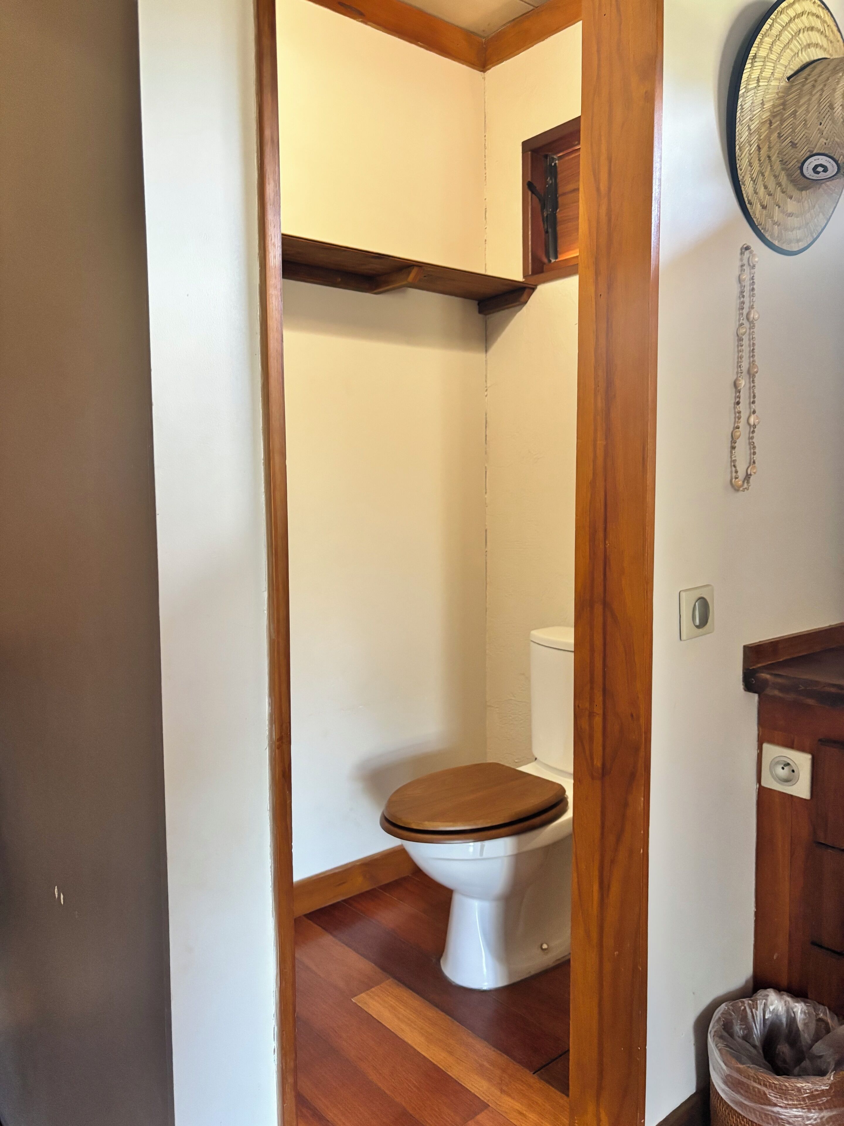 Un baño con suelo de madera, inodoro blanco y tocador de madera con un cubo de basura.
