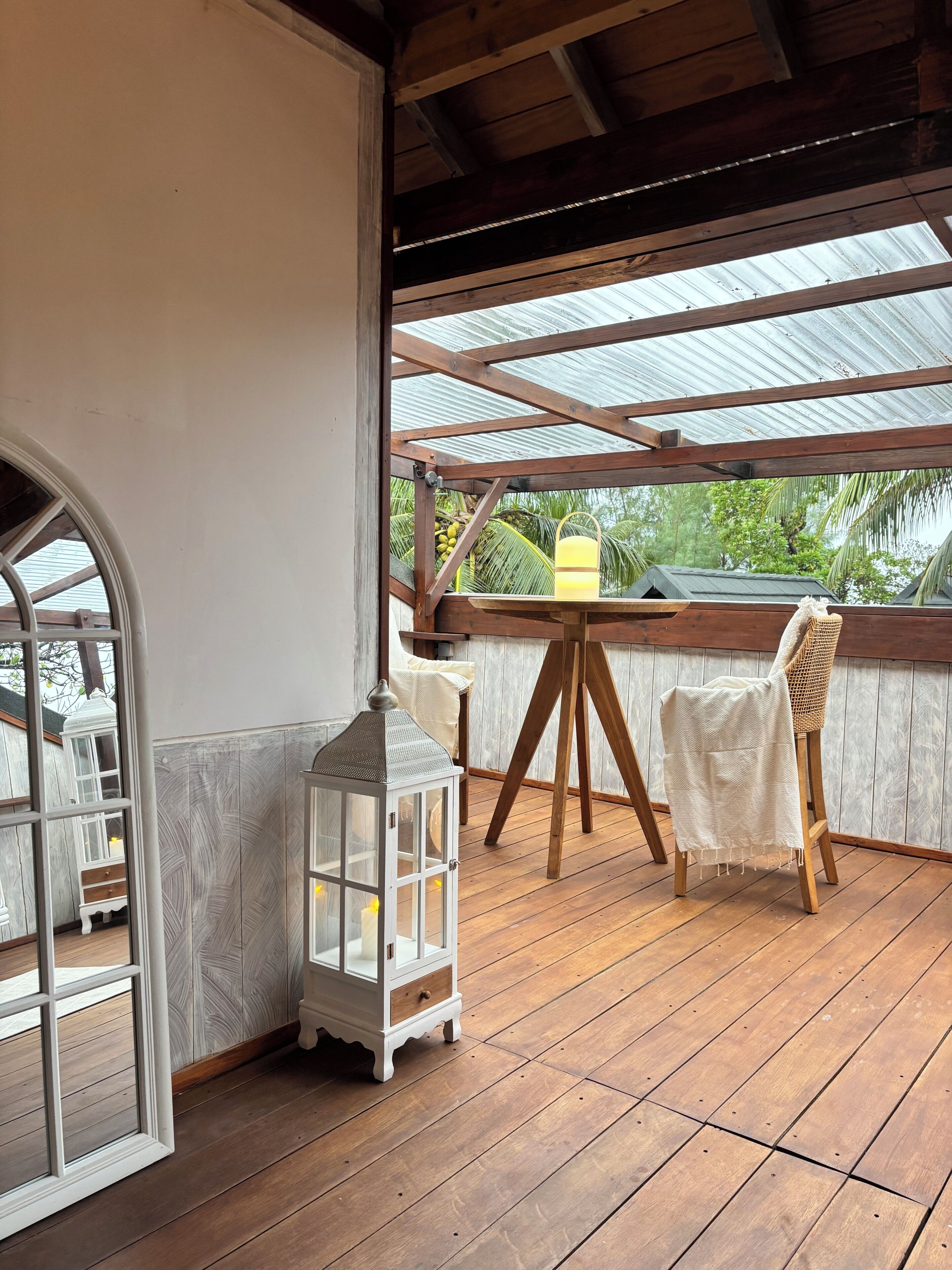 A wooden deck with a white lantern, a wicker chair, and a table with a cloth.