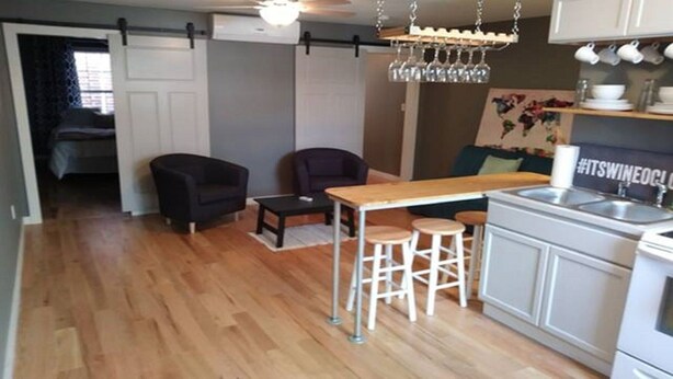 A compact kitchen with a bar area, a dining table with stools, and a small seating area with two chairs. - Wine Alley East suite (Hermann)