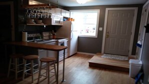A kitchen with a wooden bar, stools, a refrigerator, and a window with a view. - Wine Alley East suite (Hermann)