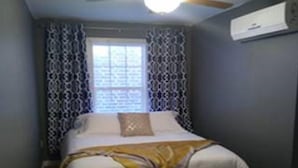 A bedroom with a bed, a ceiling fan, a window with patterned curtains, and an air conditioning unit on the wall. - Wine Alley East suite (Hermann)