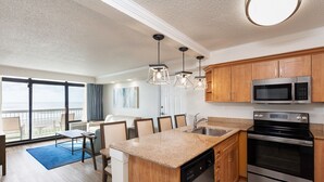 A modern kitchen with wooden cabinets, stainless steel appliances, and a dining area with a blue rug. -  Special Exceptional Offer Guaranteed Oceanfront Villa  Available July 11-18 (Myrtle Beach)