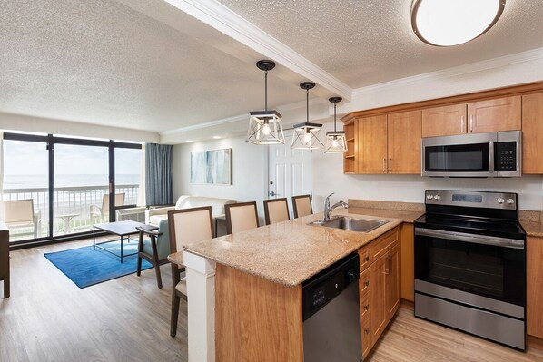 A modern kitchen with wooden cabinets, stainless steel appliances, and a dining area with a blue rug.