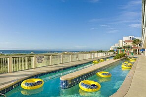 Una piscina amb anells inflables grocs, un pont de fusta i vista a l'oceà.