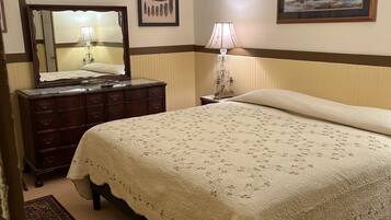 A bedroom with a large bed, a dresser, a mirror, a chandelier, and a framed picture on the wall.