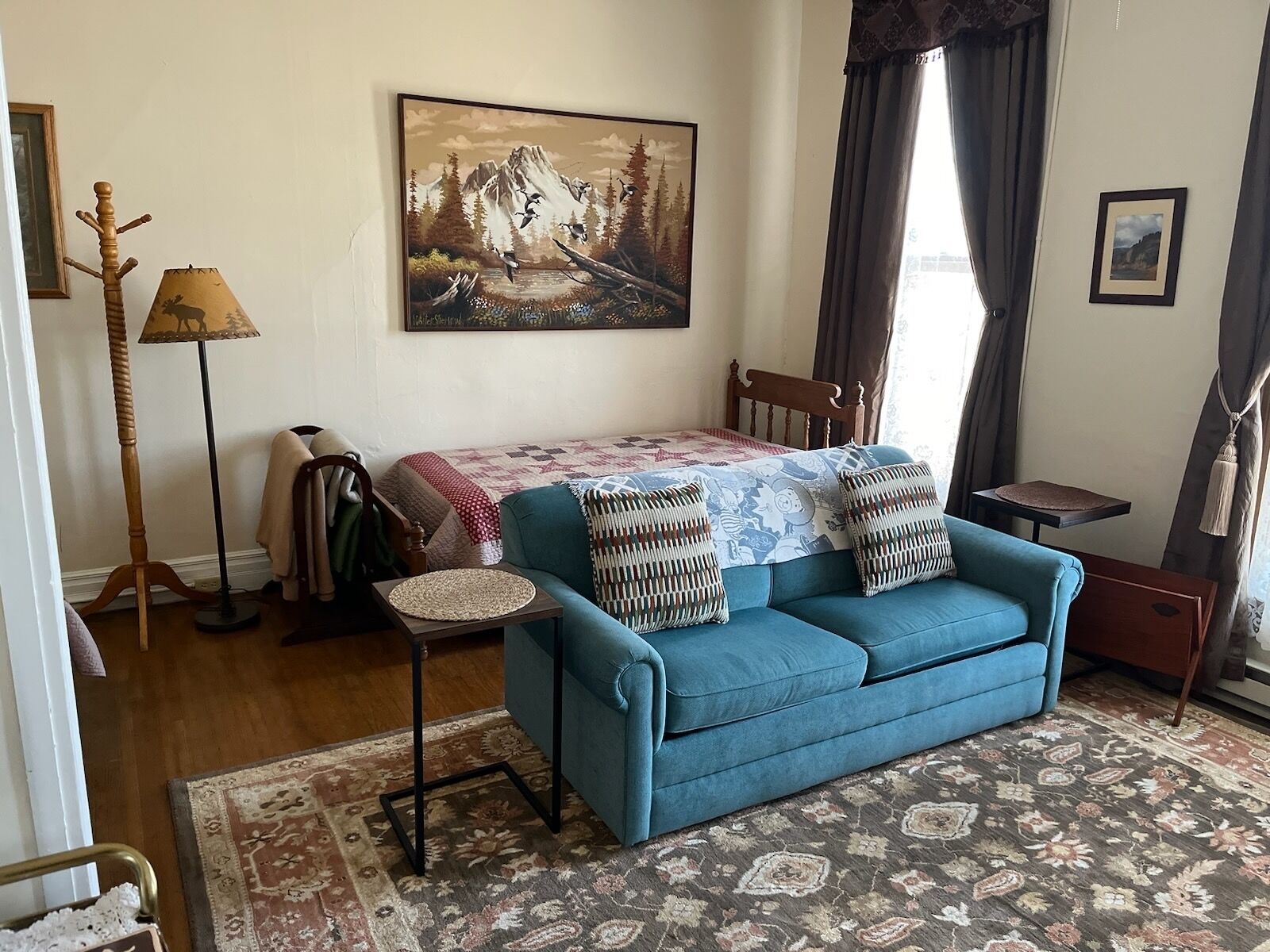 A cozy living room with a blue sofa, a painting of a mountain landscape, a lamp, and a small table.