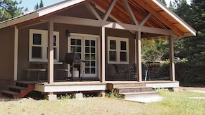 Eine kleine Holzhütte mit Veranda, Grill und Fenster mit Tür.
