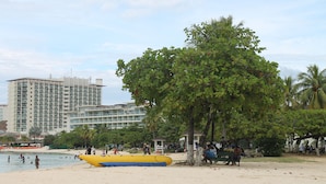 Ein Strand mit einem gelben Boot, Palmen und einem Hotel im Hintergrund.