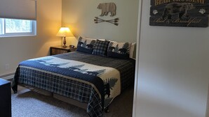 A bedroom with a bed, a nightstand with a lamp, a window, and a wall decoration of a bear crossing sign. - 3 Bedroom, 1 Bath Peaceful Lodge Just Minutes From The Kenai River and Soldotna! (Soldotna)
