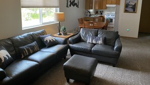 A living room with a sectional sofa, a dining table, and a kitchen in the background. - 3 Bedroom, 1 Bath Peaceful Lodge Just Minutes From The Kenai River and Soldotna! (Soldotna)