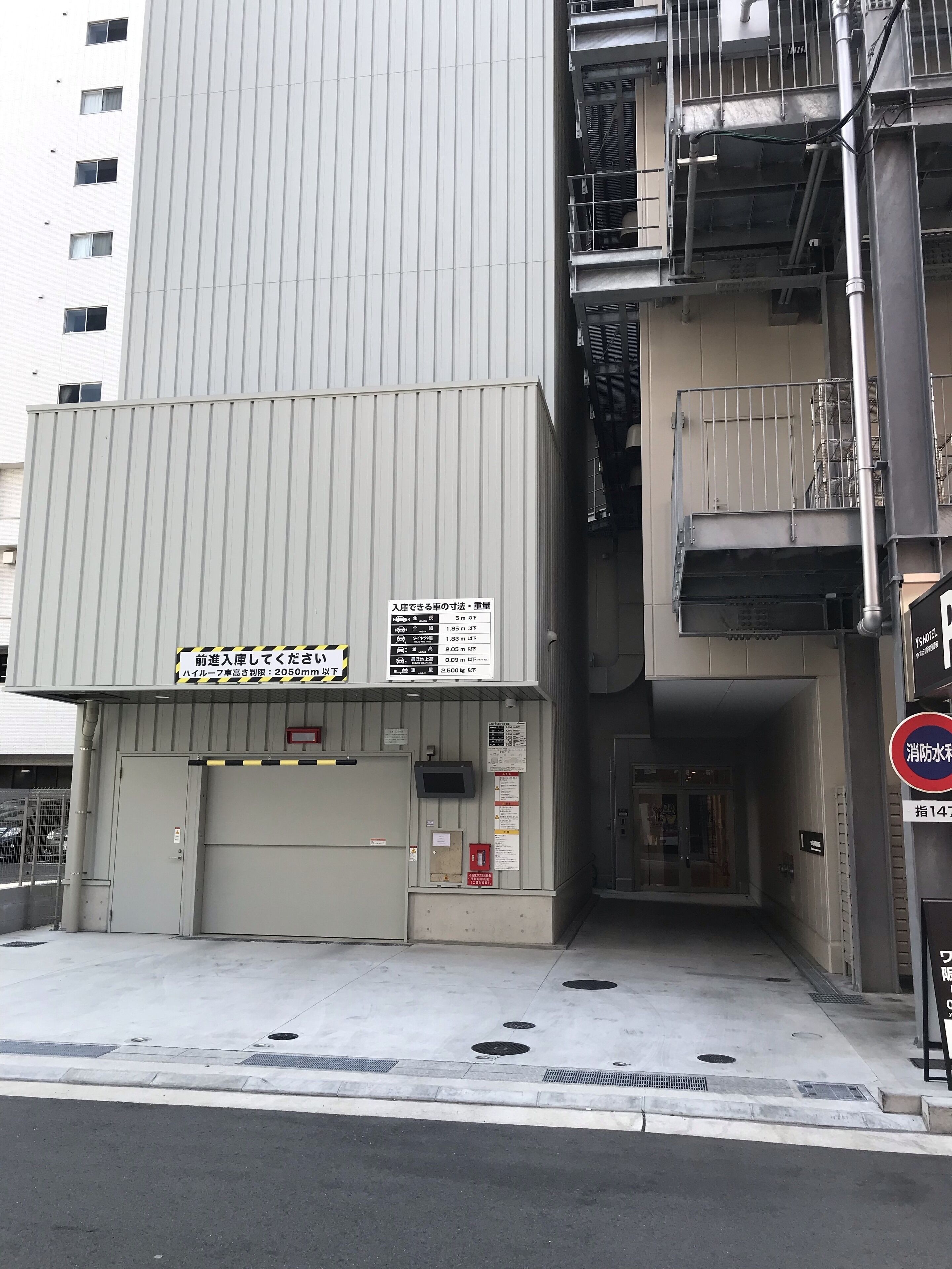 Ein mehrstöckiges Gebäude mit grauer Fassade, einem Brandschutztreppe und einem Garageneingang.