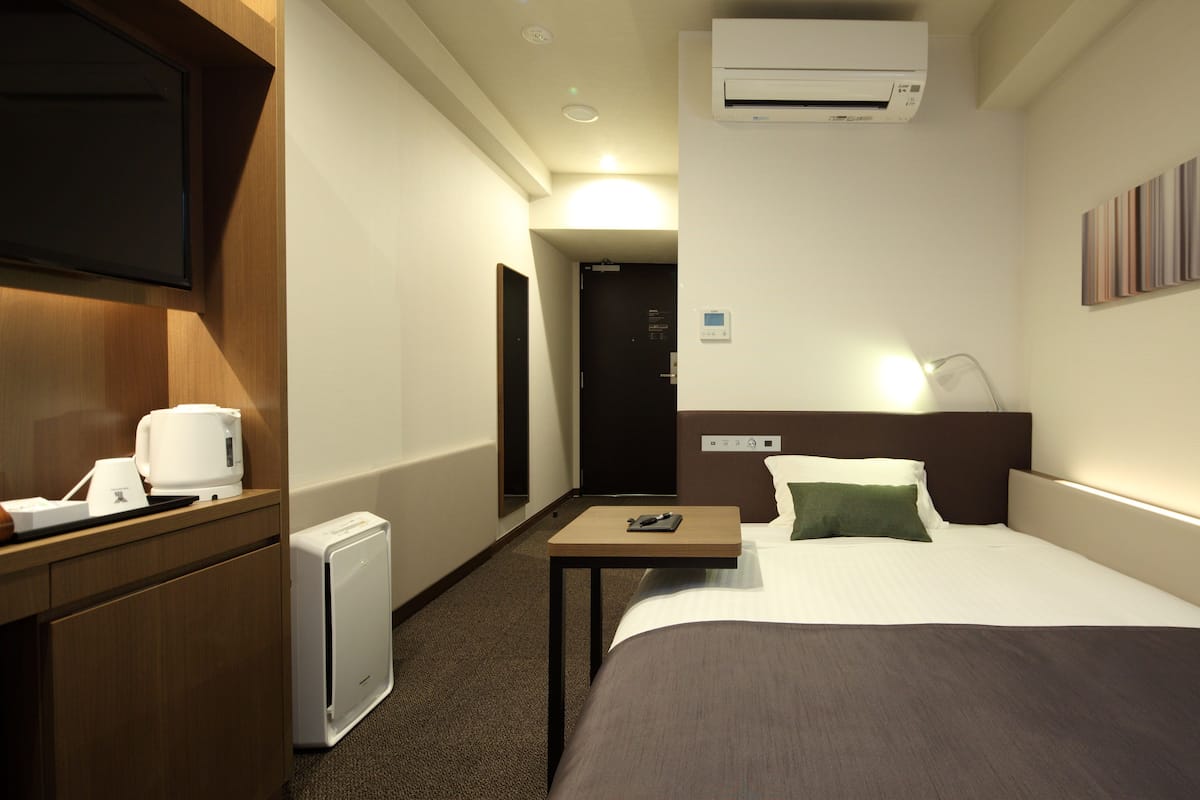 Habitación de hotel con cama, mesita de noche, televisión y una pequeña zona de kitchenette.