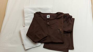 A neatly folded brown shirt and a white towel on a bed.