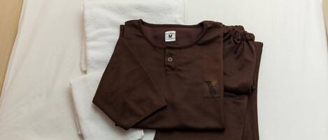 A neatly folded brown shirt and a white towel on a bed.