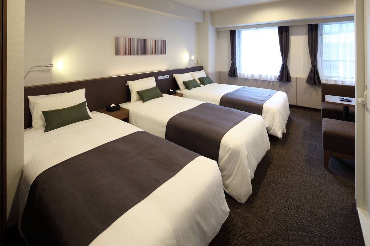 Habitación de hotel con dos camas, un escritorio y una ventana con cortinas.