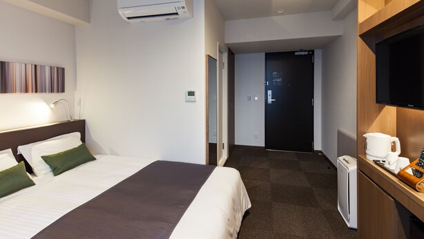A hotel room with a bed, a desk with a coffee maker, and a TV.