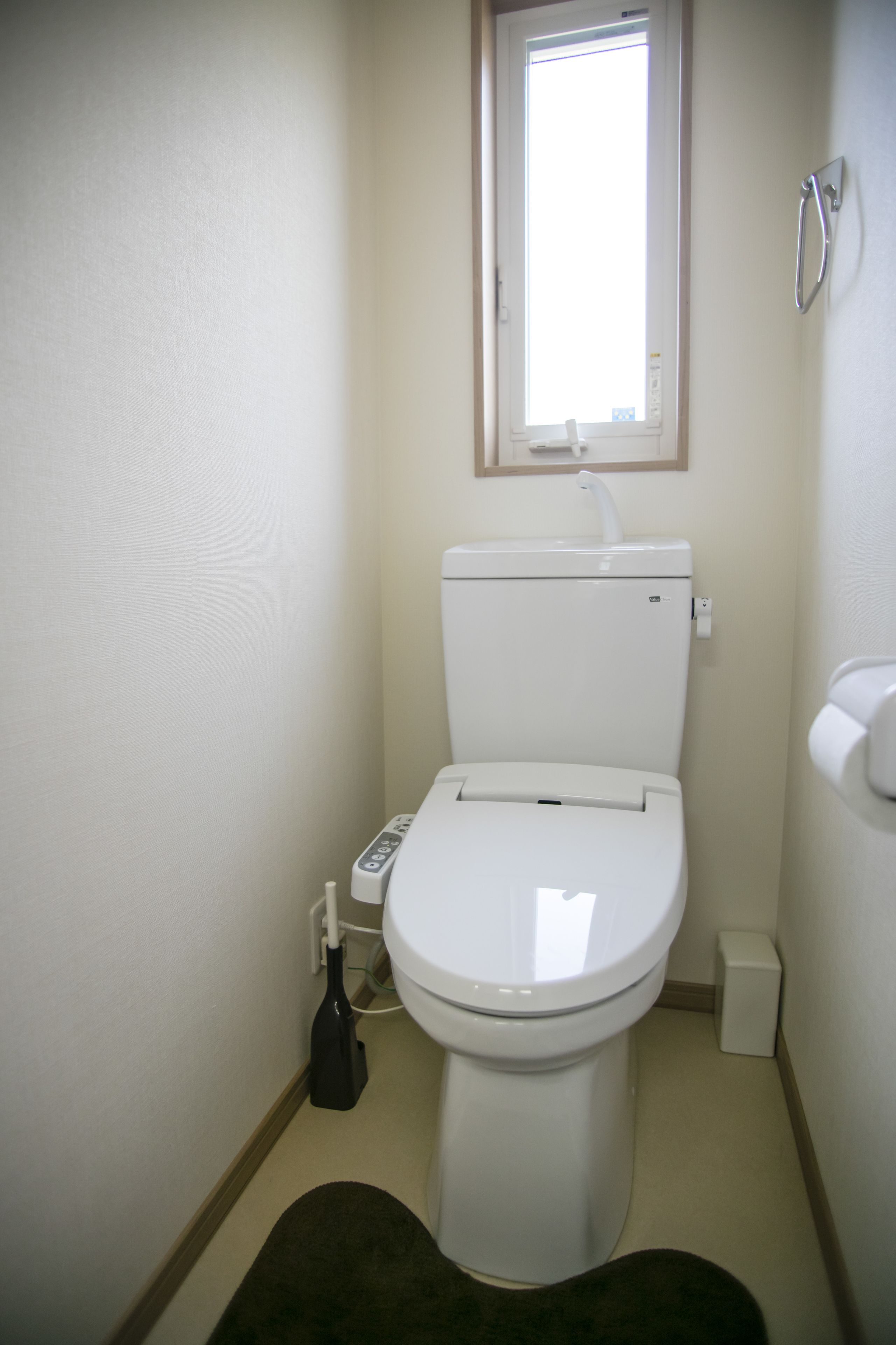A small, compact bathroom with a white toilet, a window above the toilet, and a small trash bin to the right.