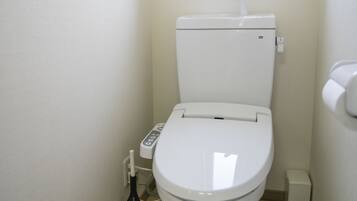 A small, compact bathroom with a white toilet, a window above the toilet, and a small trash bin to the right.
