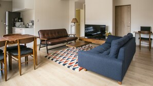 A modern living room with a sofa, coffee table, dining table, and chairs. A television is mounted on the wall. - Koko (Fujikawaguchiko)