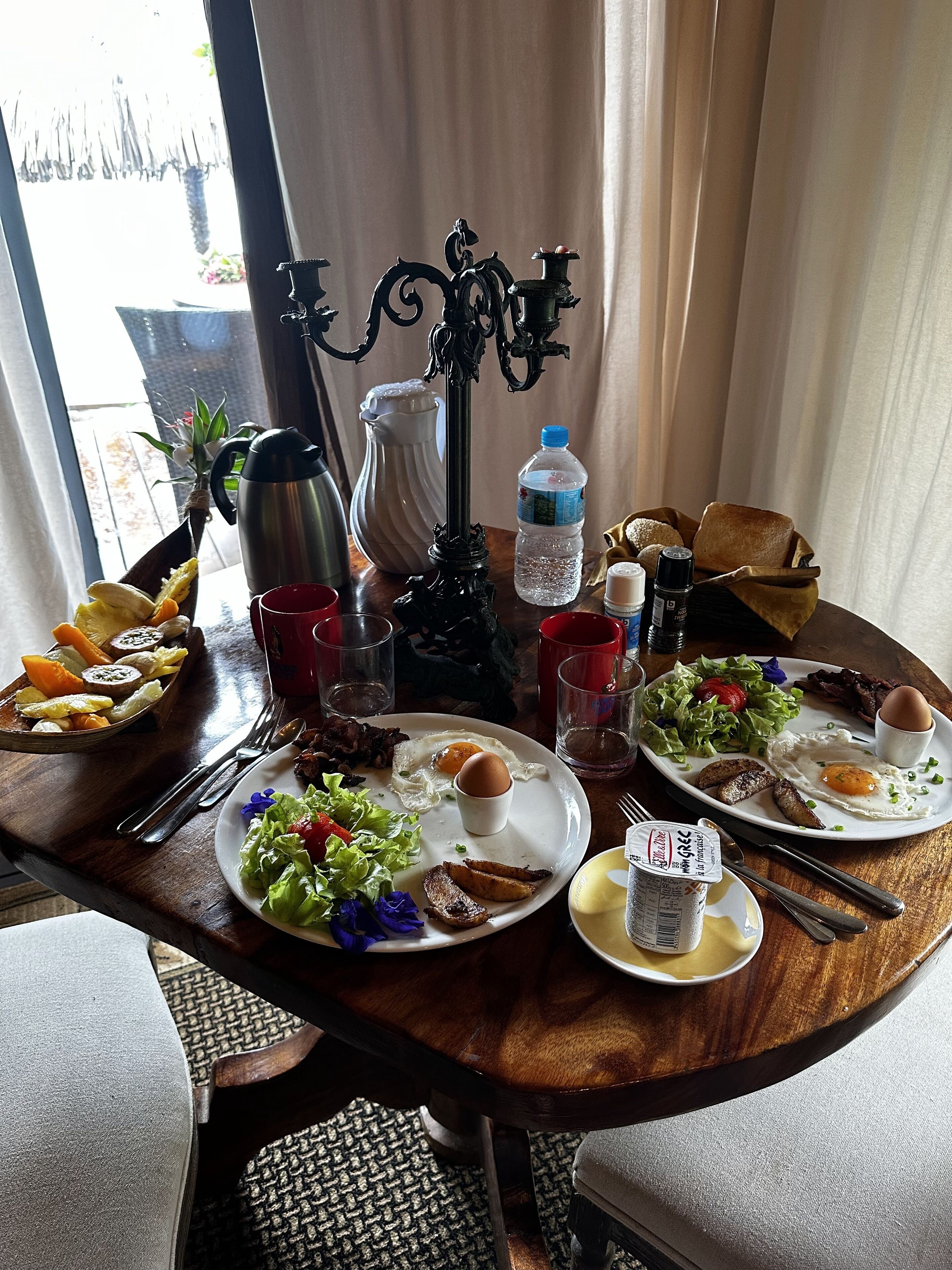 Una mesa de desayuno con platos de huevos, tocino y tostadas, una botella de agua y una cafetera.