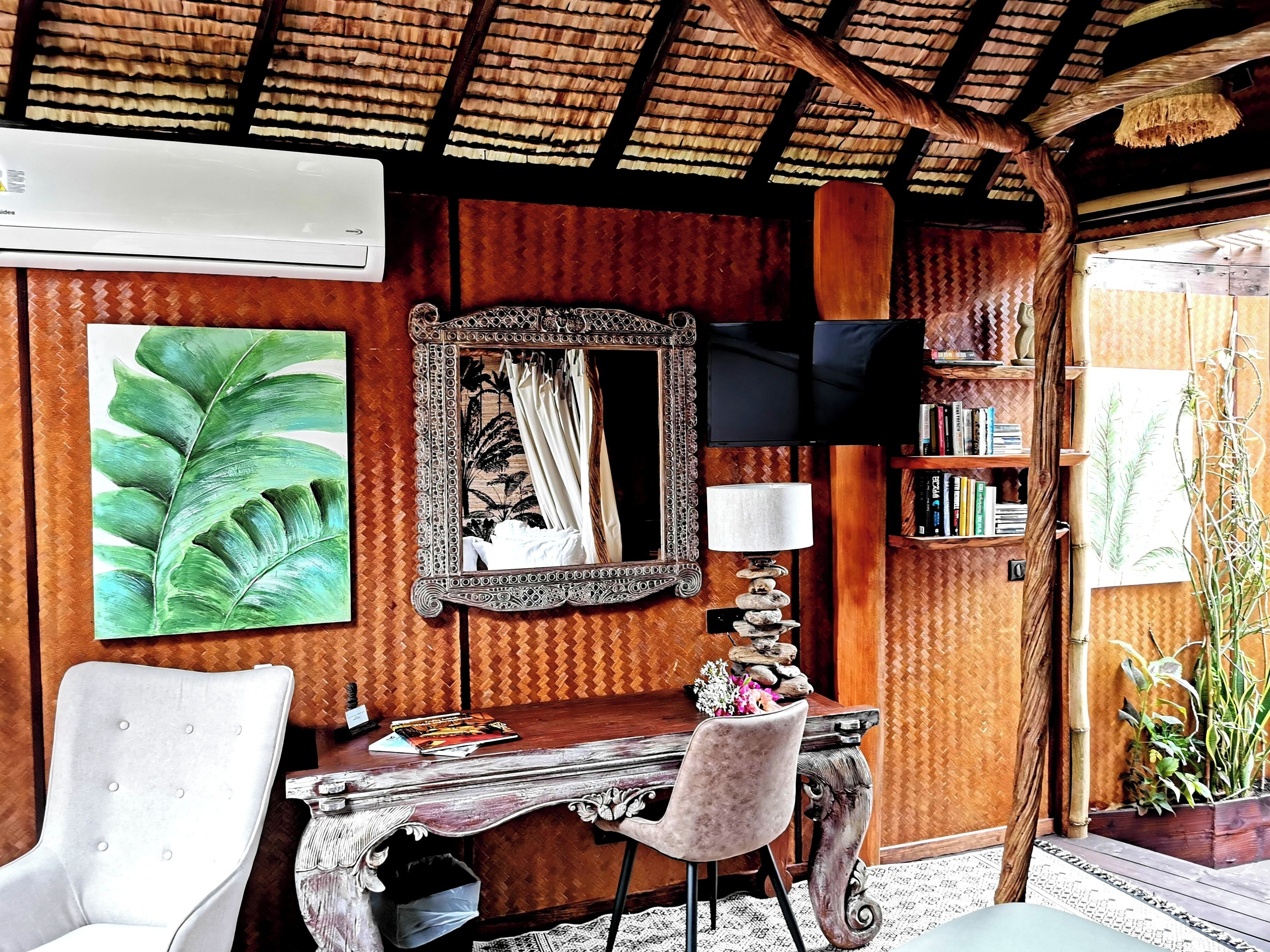 A room with a wooden desk, a chair, a mirror, a television, and a bookshelf.