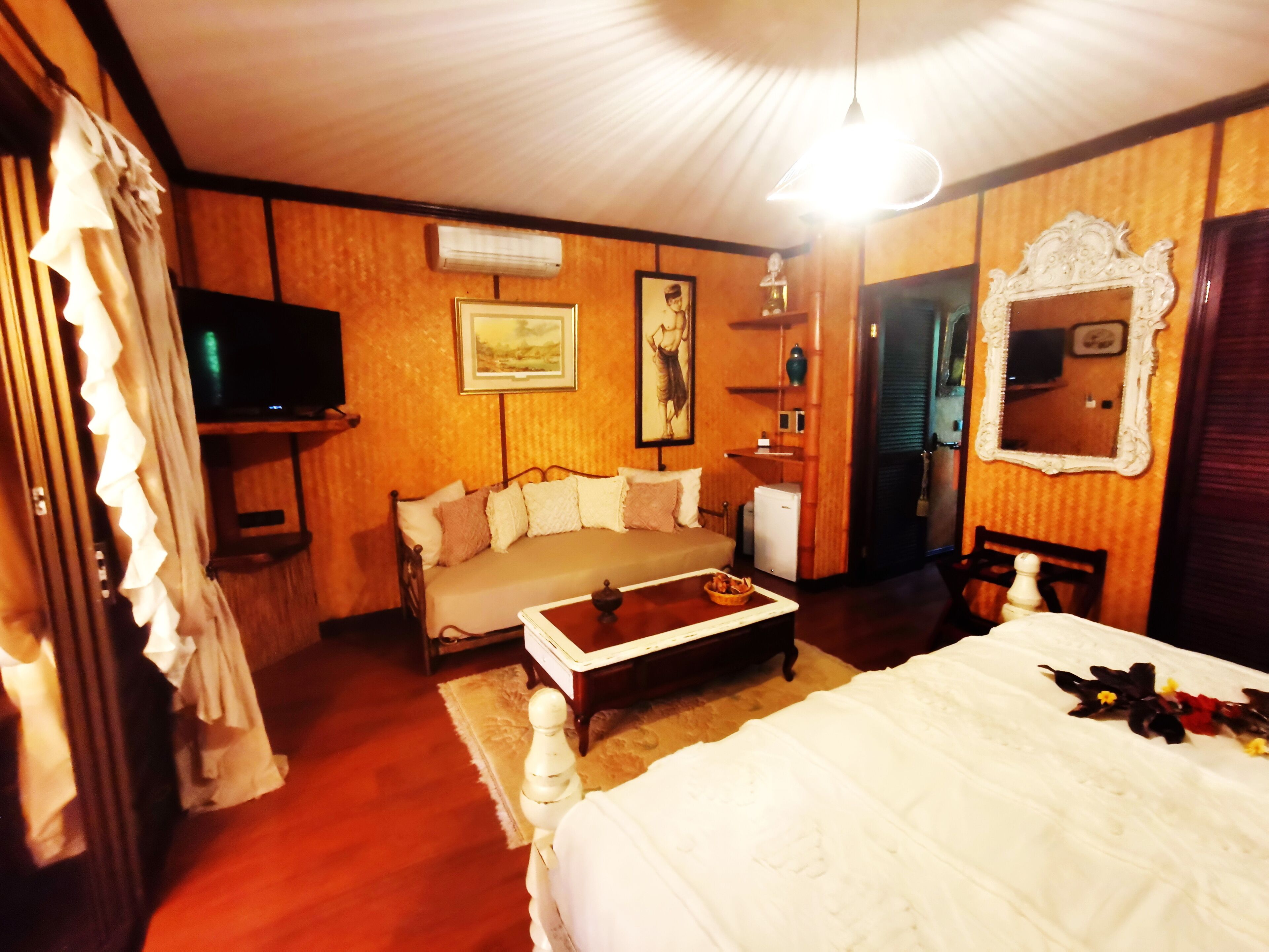 A cozy room with a bed, a sofa, a television, and a mirror.