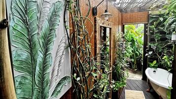 A wooden deck with a rustic brick wall, a large leaf mural, and a vintage bathtub.